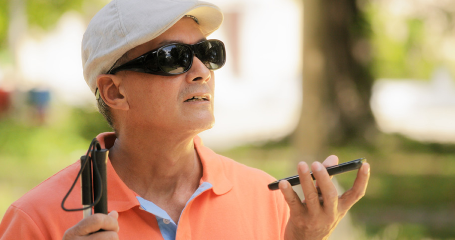 blind man wearing sunglasses and golfers hat caring white cane and  holding a cell phone