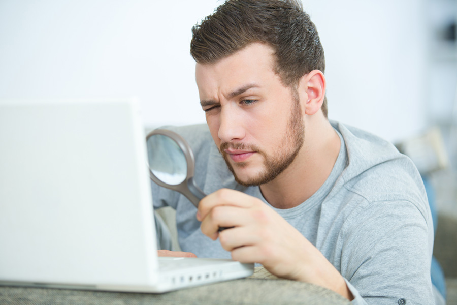 man using a magnifying glass to view laptop